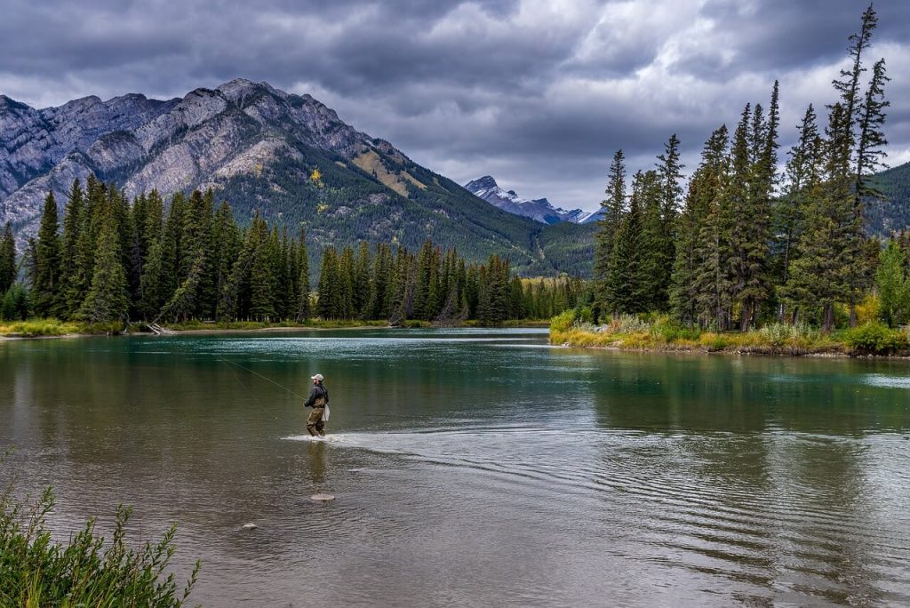Pêcheur dans une rivière avec des montagnes au loin.